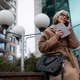A woman in a coat talks on her phone while holding a notebook outside a modern building in an urban A woman in a coat talks on her phone while holding a notebook outside a modern building in an urban - PhotoDune Item for Sale