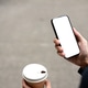 Close up of a man's hand holding coffee looking at white screen smartphone while standing on street. Close up of a man's hand holding coffee looking at white screen smartphone while standing on street. - PhotoDune Item for Sale