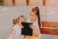 Two sisters girls sitting in park and using gadget tablet pad. Wireless technologies Two sisters girls sitting in park and using gadget tablet pad. Wireless technologies - PhotoDune Item for Sale