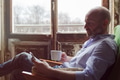 A man drinks coffee and checks the news in the phone, sitting in a chair by the window A man drinks coffee and checks the news in the phone, sitting in a chair by the window - PhotoDune Item for Sale