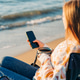 Young beautiful woman holding texting smartphone cellphone while drinking coffee on winter beach Young beautiful woman holding texting smartphone cellphone while drinking coffee on winter beach - PhotoDune Item for Sale