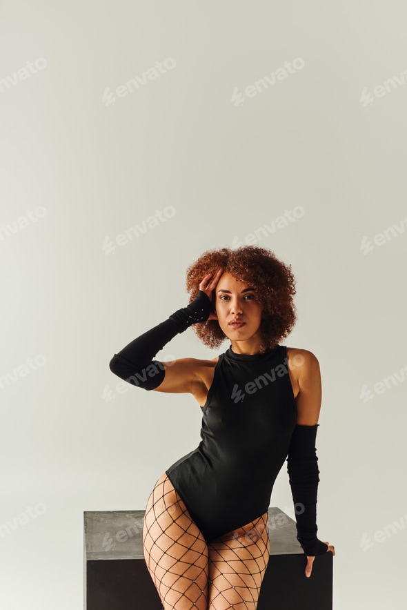 appealing african american woman in fishnet tights and sexy bodysuit posing near black cube, fashion Stock Photo by LightFieldStudios appealing african american woman in fishnet tights and sexy bodysuit posing near black cube, fashion Stock Photo by LightFieldStudios