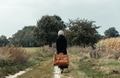 Stylish woman in black coat and suitcase walking down on countryside road Stylish woman in black coat and suitcase walking down on countryside road - PhotoDune Item for Sale