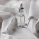 Glass dropper bottle with clear liquid on white satin fabric Glass dropper bottle with clear liquid on white satin fabric - PhotoDune Item for Sale