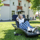 A blonde woman with a laptop works in the garden on a sun lounger, home office concept. A blonde woman with a laptop works in the garden on a sun lounger, home office concept. - PhotoDune Item for Sale
