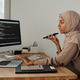 Side view of confident Muslim female programmer talking by speakerphone ...