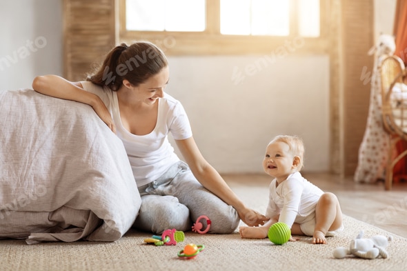 Happy mom sitting on floor play with baby at home Stock Photo by