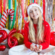 Smiling young girl in Christmas sweater and Santa hat sitting among festive decorations Smiling young girl in Christmas sweater and Santa hat sitting among festive decorations - PhotoDune Item for Sale