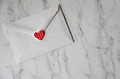Overhead view of minimalistic white envelope with red heart on a marble surface for Valentines Day. Overhead view of minimalistic white envelope with red heart on a marble surface for Valentines Day. - PhotoDune Item for Sale