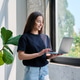 Portrait of young woman standing with laptop computer in home interior near window Portrait of young woman standing with laptop computer in home interior near window - PhotoDune Item for Sale