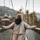 Beautiful young woman traveler on a suspension bridge enjoys view on autumn mountains and church Beautiful young woman traveler on a suspension bridge enjoys view on autumn mountains and church - PhotoDune Item for Sale