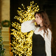 woman in a white blouse stands in profile against the backdrop of a Christmas tree with garland. woman in a white blouse stands in profile against the backdrop of a Christmas tree with garland. - PhotoDune Item for Sale