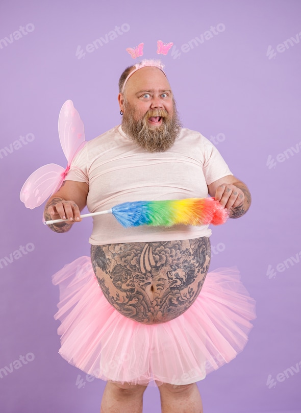 Bearded plump man in fairy costume holds colorful pp duster on purple background Stock Photo by astakhovyaroslav Bearded plump man in fairy costume holds colorful pp duster on purple background Stock Photo by astakhovyaroslav