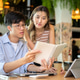 Asian woman standing and reading or looking at notebook in a man's hand at table in cafe or canteen. Asian woman standing and reading or looking at notebook in a man's hand at table in cafe or canteen. - PhotoDune Item for Sale