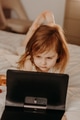 Toddler girl lying in bedroom, using laptop tablet pad gadget, watching with focused face, vertical Toddler girl lying in bedroom, using laptop tablet pad gadget, watching with focused face, vertical - PhotoDune Item for Sale