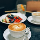 Delicious cappuccino with latte art on table in cafe with fruit plate and iced drink Delicious cappuccino with latte art on table in cafe with fruit plate and iced drink - PhotoDune Item for Sale