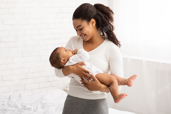 Black Mom Holding Baby In Arms Standing In Bedroom Indoor Stock