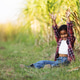 A joyful young child sits on green grass near a sugarcane field with arms raised in celebration A joyful young child sits on green grass near a sugarcane field with arms raised in celebration - PhotoDune Item for Sale