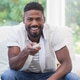 African American man sitting on white sofa by large window holding remote control and smiling African American man sitting on white sofa by large window holding remote control and smiling - PhotoDune Item for Sale