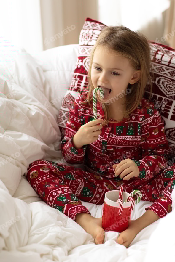 Cute little girl in Christmas pajamas licking candy