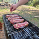 Person seasoning steaks on grill at outdoor picnic, surrounded by forest, preparing meat Person seasoning steaks on grill at outdoor picnic, surrounded by forest, preparing meat - PhotoDune Item for Sale