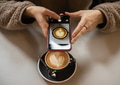 Girl in fluffy sweater holds a smartphone in hands and takes a photo of a cup of coffee with heart Girl in fluffy sweater holds a smartphone in hands and takes a photo of a cup of coffee with heart - PhotoDune Item for Sale