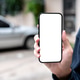 Close up of man's hand holding and showing white screen smartphone while standing in parking lot. Close up of man's hand holding and showing white screen smartphone while standing in parking lot. - PhotoDune Item for Sale