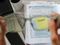Person holding glasses focusing on yellow sticky note with word Taxes on tax forms and documents Person holding glasses focusing on yellow sticky note with word Taxes on tax forms and documents - PhotoDune Item for Sale