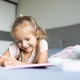Young girl drawing with a pink pencil while lying on a bed indoors Young girl drawing with a pink pencil while lying on a bed indoors - PhotoDune Item for Sale