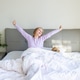 Happy young girl stretching arms while waking up in bed at home Happy young girl stretching arms while waking up in bed at home - PhotoDune Item for Sale