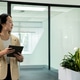 Chinese woman wearing beige blazer standing by planters in office holding black tablet, copy space Chinese woman wearing beige blazer standing by planters in office holding black tablet, copy space - PhotoDune Item for Sale
