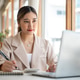 Asian woman holding pen over notebook as looking and typing on laptop sits with coffee at cafe table Asian woman holding pen over notebook as looking and typing on laptop sits with coffee at cafe table - PhotoDune Item for Sale