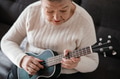 Elderly woman 70+ sits on the couch at home and plays the ukulele Elderly woman 70+ sits on the couch at home and plays the ukulele - PhotoDune Item for Sale