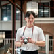 Asian man wearing glasses in white t shirt is standing and holding his camera in cafe or coffee shop Asian man wearing glasses in white t shirt is standing and holding his camera in cafe or coffee shop - PhotoDune Item for Sale
