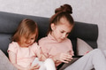 Two little girls sisters sitting in bedroom, holding gadgets. Kids using technologies at home Two little girls sisters sitting in bedroom, holding gadgets. Kids using technologies at home - PhotoDune Item for Sale