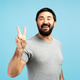 Happy bearded man showing victory sign on blue background Happy bearded man showing victory sign on blue background - PhotoDune Item for Sale