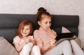 Two little girls sisters sitting in bedroom, holding gadgets. Kids using technologies at home Two little girls sisters sitting in bedroom, holding gadgets. Kids using technologies at home - PhotoDune Item for Sale