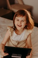 Toddler girl sitting in bedroom, using laptop tablet pad gadget, watching with sincere smiling face Toddler girl sitting in bedroom, using laptop tablet pad gadget, watching with sincere smiling face - PhotoDune Item for Sale