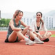 Asian woman holding water bottle talking to a friend as sitting on racetrack resting after running. Asian woman holding water bottle talking to a friend as sitting on racetrack resting after running. - PhotoDune Item for Sale