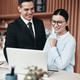Two smiling businesspeople using a laptop together in an office Two smiling businesspeople using a laptop together in an office - PhotoDune Item for Sale