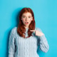 Confused redhead girl pointing at herself, being chosen, standing in sweater against blue Confused redhead girl pointing at herself, being chosen, standing in sweater against blue - PhotoDune Item for Sale