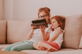 Sharing secrets and news with friends. Two little girls on couch. Kids using tablet pad technologies Sharing secrets and news with friends. Two little girls on couch. Kids using tablet pad technologies - PhotoDune Item for Sale