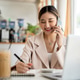 Asian woman talking on phone with pen on notebook as sitting with laptop and coffee at cafe's table. Asian woman talking on phone with pen on notebook as sitting with laptop and coffee at cafe's table. - PhotoDune Item for Sale