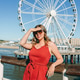Woman in red dress posing near ferris wheel by seaside, looking and smiling Woman in red dress posing near ferris wheel by seaside, looking and smiling - PhotoDune Item for Sale