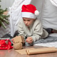 Gift wrapping. A child in a red Santa hat wraps Christmas gifts surprises in kraft paper Gift wrapping. A child in a red Santa hat wraps Christmas gifts surprises in kraft paper - PhotoDune Item for Sale