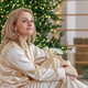 A blonde woman in pajamas sits on the living room floor. Christmas decorations, New Year. A blonde woman in pajamas sits on the living room floor. Christmas decorations, New Year. - PhotoDune Item for Sale