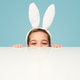 Playful girl in bunny ears hiding behind table Playful girl in bunny ears hiding behind table - PhotoDune Item for Sale
