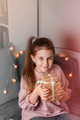 Preteen girl sitting in bedroom, holding gift boxes above lights decoration, Christmas holiday Preteen girl sitting in bedroom, holding gift boxes above lights decoration, Christmas holiday - PhotoDune Item for Sale