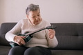 Elderly woman 70+ sits on the couch at home and tuning the ukulele Elderly woman 70+ sits on the couch at home and tuning the ukulele - PhotoDune Item for Sale