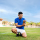 Asian man in blue shirt holding and looking at his arm while kneeling on grass. Arm pain or injury. Asian man in blue shirt holding and looking at his arm while kneeling on grass. Arm pain or injury. - PhotoDune Item for Sale